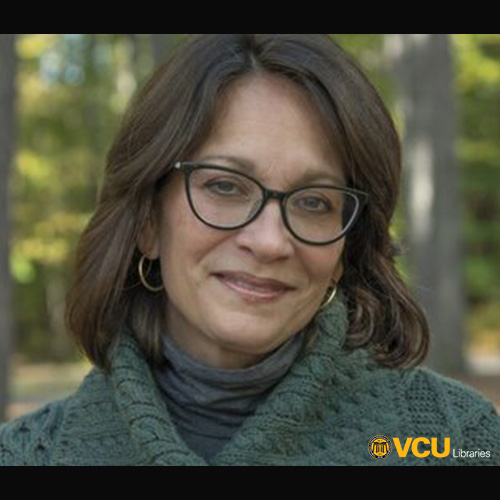 A woman with shoulder-length brown hair and glasses is smiling softly. She is wearing a green sweater and standing outdoors with blurred trees in the background. The logo for VCU Libraries is in the bottom right corner of the image.