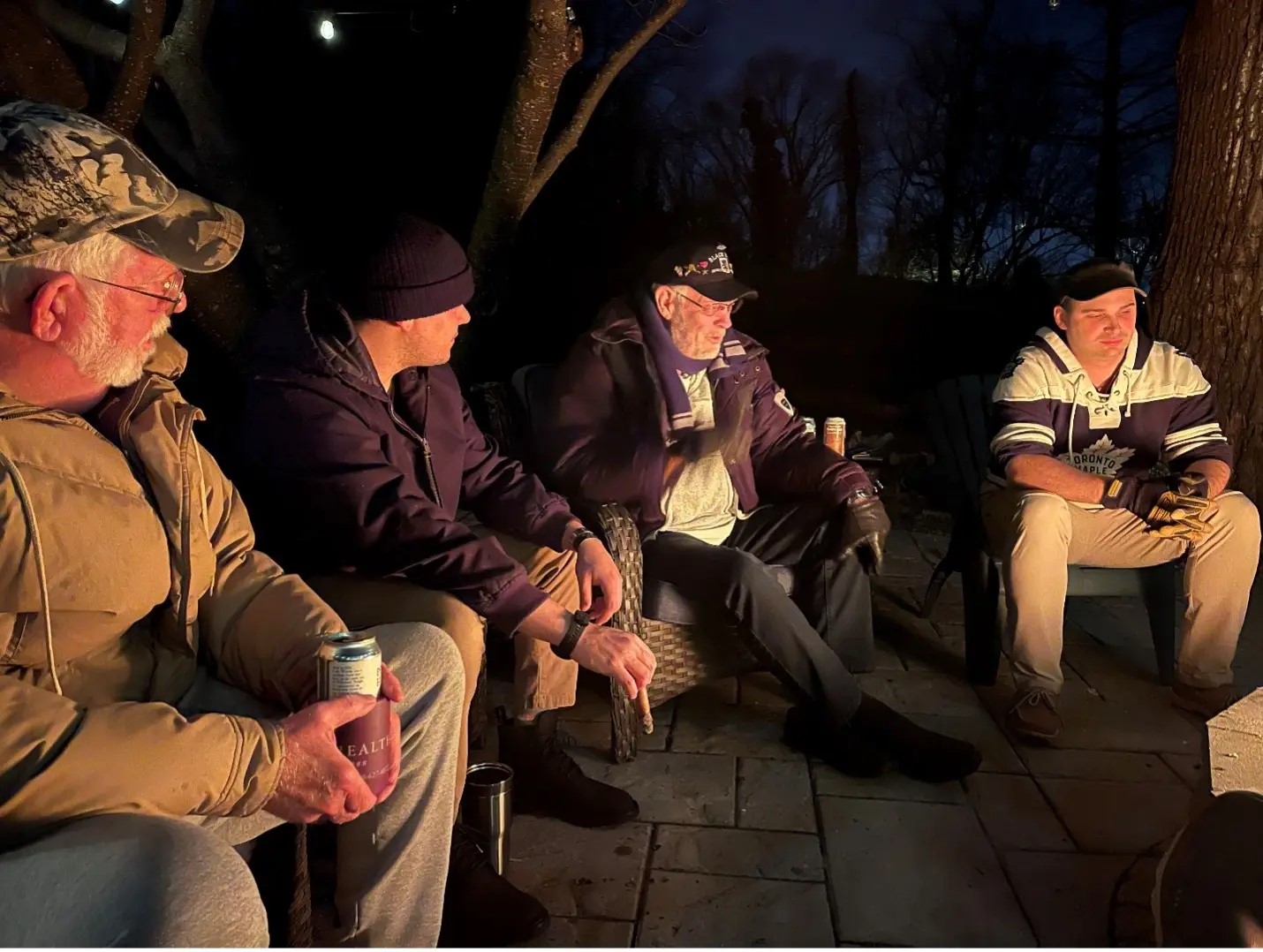 Four men sit around a firepit.